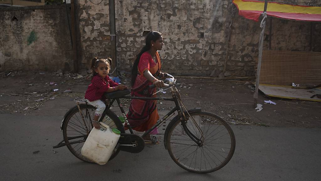 ARCHIV - Eine Frau mit einem Kind transportiert Wasser mit einem Fahrrad aus einem öffentlichen Wasserhahn in einem Slumgebiet. In Südasien leiden weltweit am meisten Kinder an Wasserknappheit. Foto: Mahesh Kumar A./AP/dpa