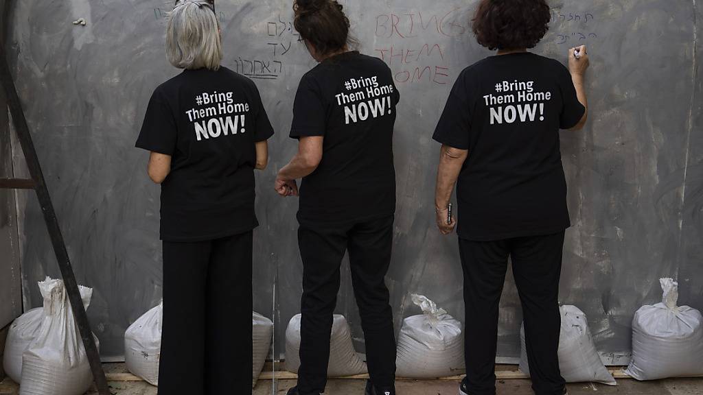 Drei Frauen schreiben auf eine Installation, die einen Tunnel im Gazastreifen simuliert, um sich mit den Geiseln zu solidarisieren, die vermutlich von der Hamas im Untergrund festgehalten werden, und fordern ihre Rückkehr. Foto: Oded Balilty/AP/dpa