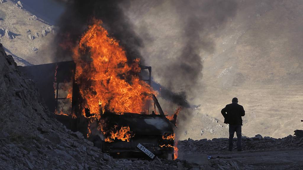 dpatopbilder - Ein Mann steht in der Nähe seines brennenden Autos, das beim Aufstieg entlang der Straße zu einem Bergpass nahe der Grenze zwischen Berg-Karabach und Armenien in Brand geraten ist. Foto: ---/AP/dpa