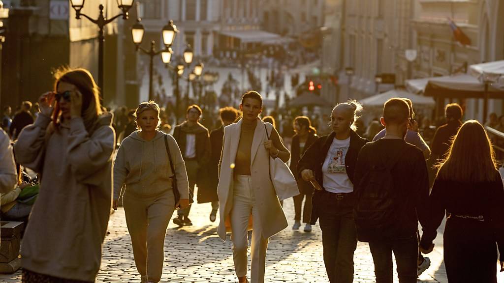 Menschen, die meisten von ihnen ohne Mund-Nasen-Schutz, spazieren bei warmem Wetter während eines Sonnenuntergangs im Zentrum von Moskau. Foto: Alexander Zemlianichenko/AP/dpa
