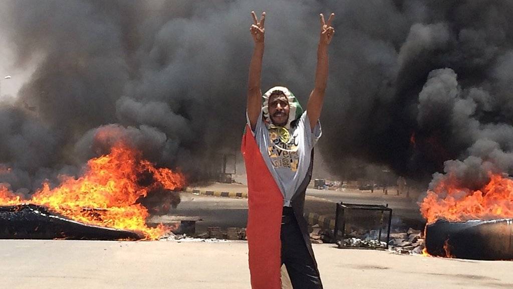 Ein Demonstrant in Khartum macht das Victory-Zeichen vor brennenden Reifen.