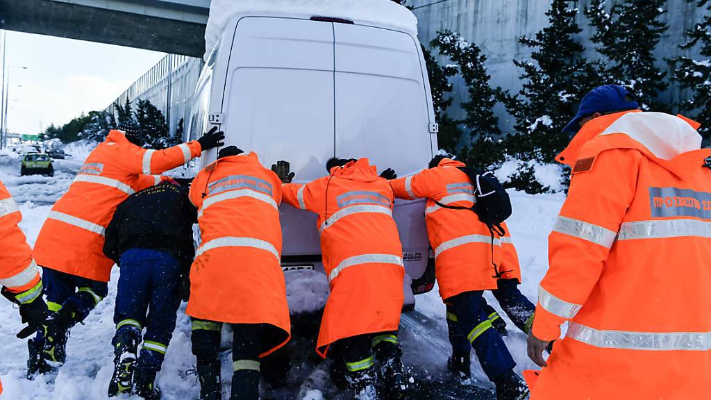 Feuerwehrleute schieben nach einem Schneesturm ein festgefahrenes Fahrzeug von einer Autobahn bei Athen. In Griechenland und der Türkei hat es nach den starken Schneefällen der vergangenen Tage auch am Dienstag weiterhin große Probleme gegeben. Foto: Michael Varaklas/AP/dpa