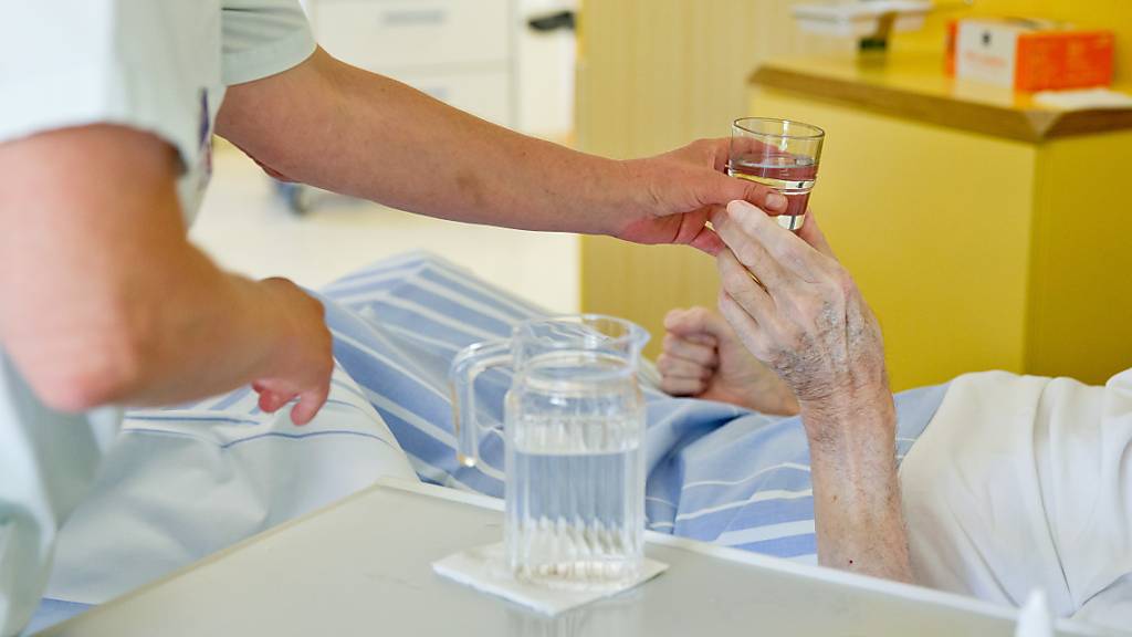 Eine Krankenpflegerin reicht einem Patienten ein Glas Wasser. 