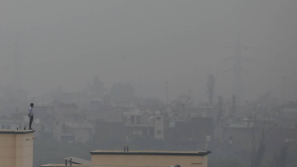 dpatopbilder - Ein Mann steht auf dem Sims eines Gebäudes in Neu Delhi, während Smog über der ganzen Stadt liegt. In der indischen Hauptstadt wurden wegen starken Smogs die Schulen von Freitag an bis auf weiteres geschlossen. Das Höchste Gericht des Landes hatte dies bereits am Donnerstag angekündigt. Foto: Altaf Qadri/AP/dpa