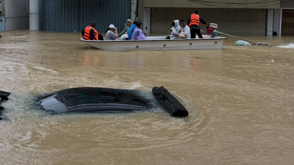 Thailändische Rettungskräfte bewegen sich auf einem Boot an einem Auto vorbei, das in der südthailändischen Provinz Songkhla in den Fluten versunken ist. Foto: Uncredited/AP/dpa