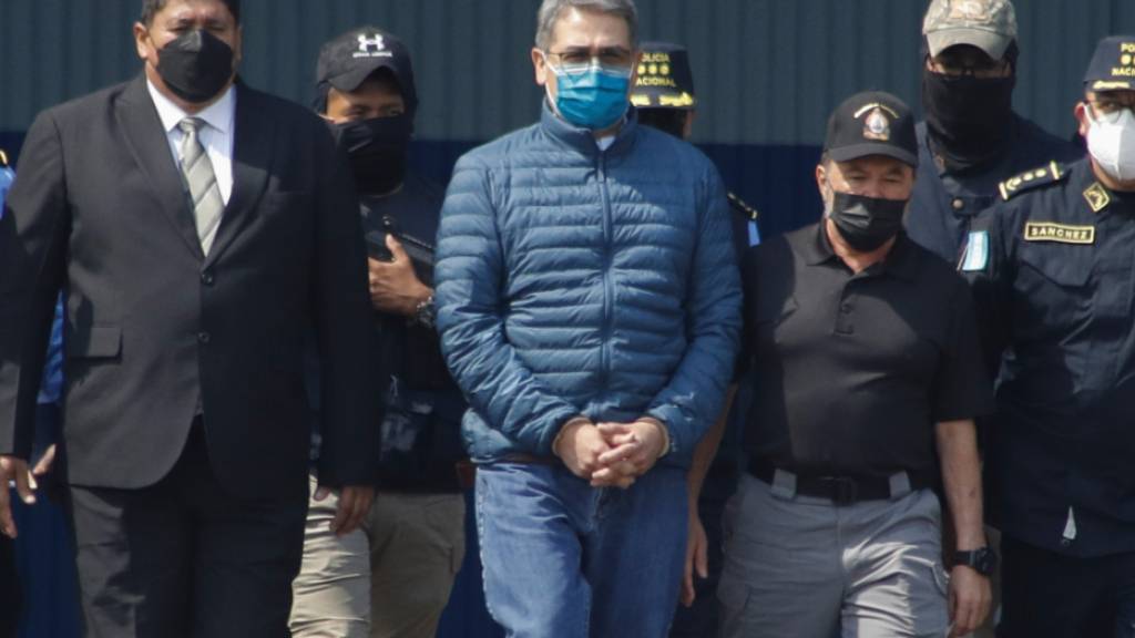 ARCHIV - Juan Orlando Hernandez (M), ehemaliger Präsident von Honduras, wird auf einem Luftwaffenstützpunkt in Handschellen zu einem wartenden Flugzeug gebracht. Foto: Elmer Martinez/AP/dpa