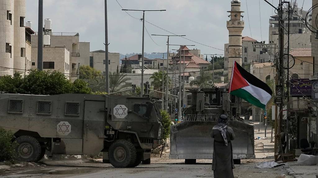 ARCHIV - Der palästinensische Aktivist Khairi Hanoon schwenkt die palästinensische Flagge, als ein Konvoi gepanzerter israelischer Militärfahrzeuge während einer Razzia der Armee in Tulkarem, Westjordanland vorbeifährt. Foto: Majdi Mohammed/AP/dpa