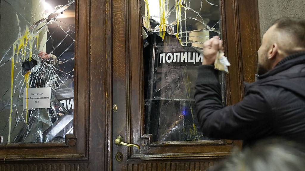 Ein Demonstrant vor einer beschädigten Tür des Rathauses. Foto: Darko Vojinovic/AP/dpa