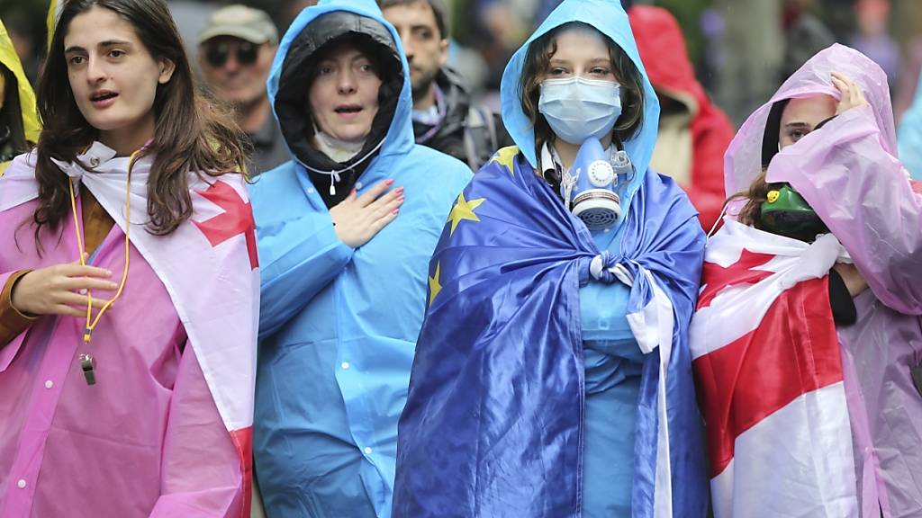 Demonstranten, die georgische National- und EU-Fahnen tragen, stehen vor einer Absperrung der Polizei während eines Protestes der Opposition gegen das «Russische Gesetz» in der Nähe des Parlamentsgebäudes. Foto: Zurab Tsertsvadze/AP/dpa