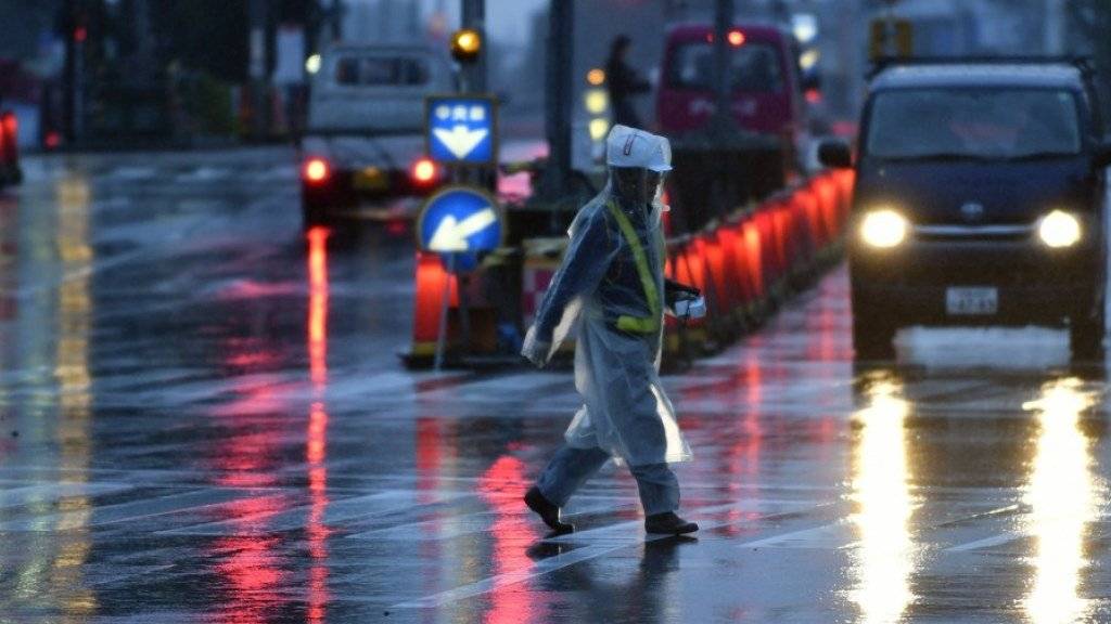 Ein Mann überquert bei Regen und starkem Wind eine Strasse in Tokio. Auch im Raum der japanischen Hauptstadt schwollen wegen Taifun «Lan» Flüsse an.