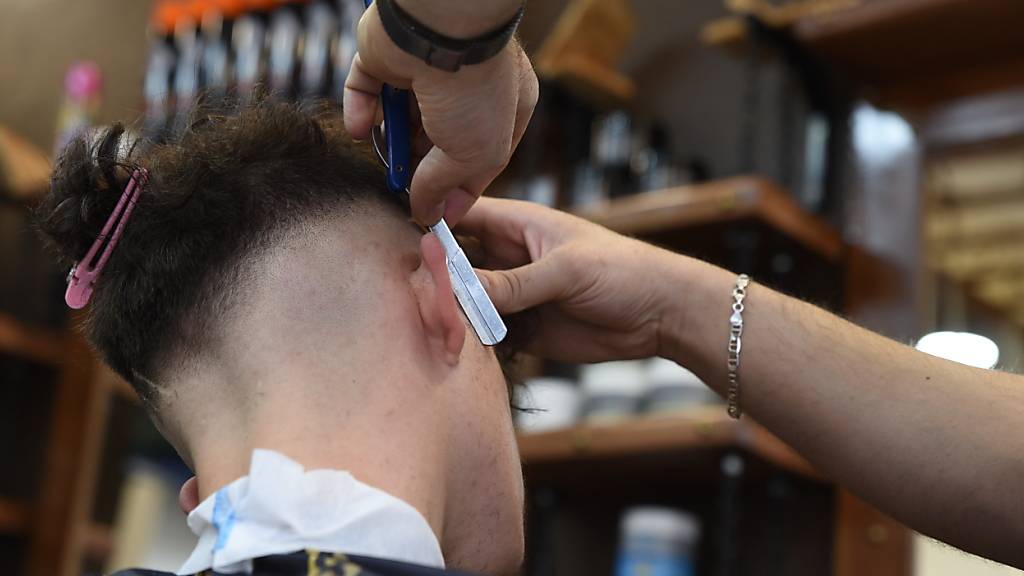 Ein Friseur rasiert in einem Barbershop die Haare eines männlichen Kunden. (Symbolbild)