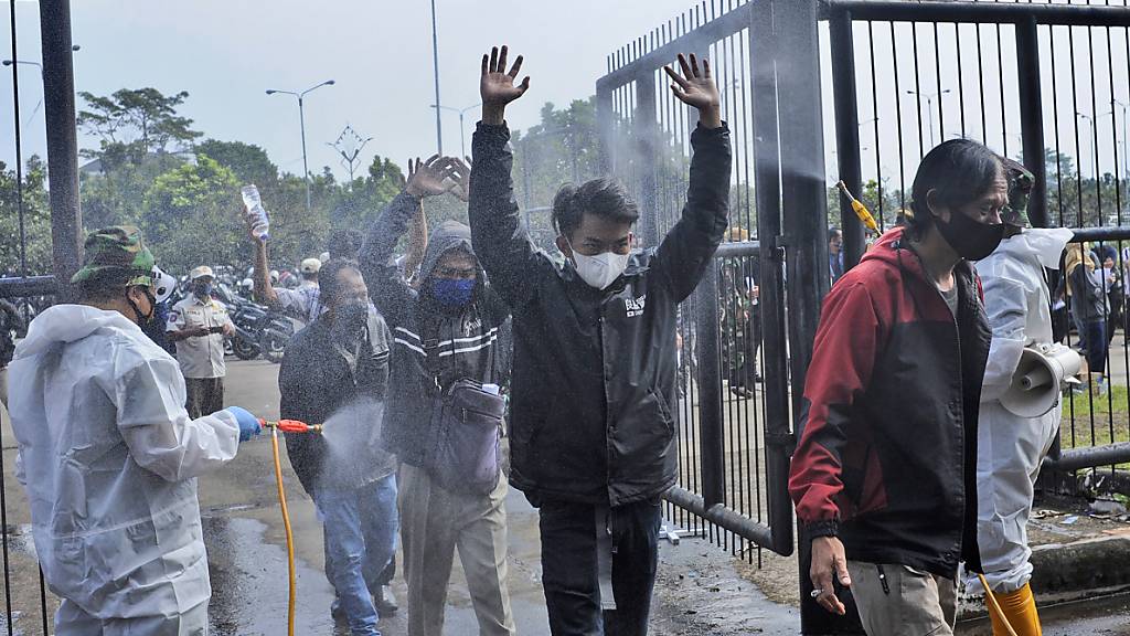 Soldaten in Schutzanzügen sprühen Desinfektionsmittel auf Menschen, die das Stadion Gelora Bandung Lautan Api Stadion betreten, um gegen den Coronavirus impfen zu lassen. Foto: Bukbis Candra/AP/dpa