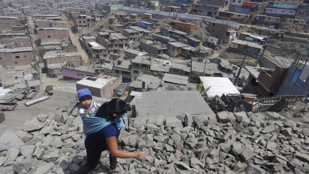 ARCHIV - Eine Frau trägt ihr Kind am Rücken und geht über Steine zu einem Haus in Lima, in dem Essen verteilt wird. Foto: Gian Masko/dpa
