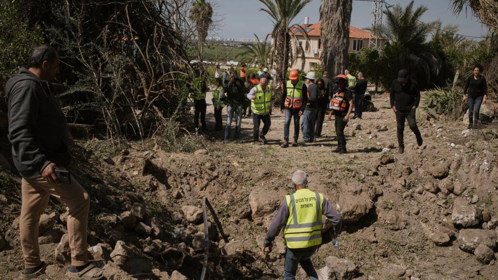 Anwohner und israelische Sicherheitskräfte inspizieren den Einschlagsort einer iranischen Rakete in Zentralisrael. Foto: Leo Correa/AP/dpa