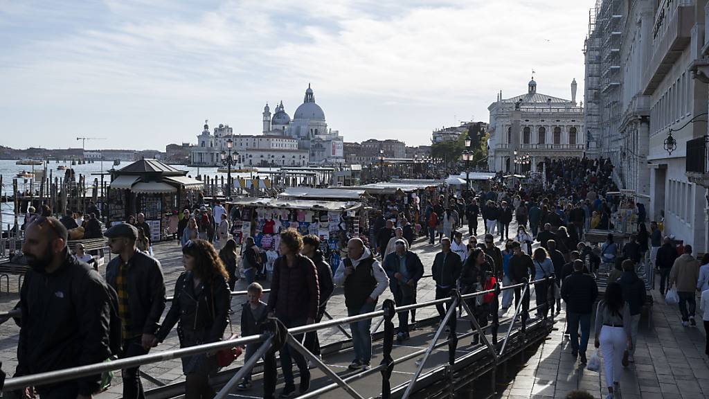Touristen schlendern an der Sonne durch Venedig, im Hintergrund die Basilika Santa Maria della Salute. (Archivbild)