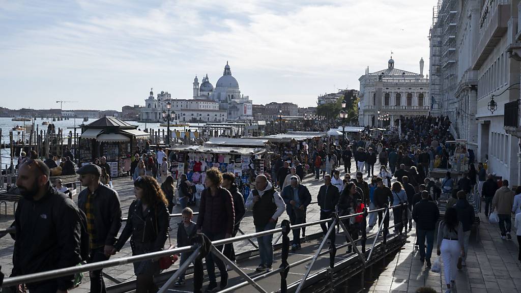 Touristen schlendern an der Sonne durch Venedig, im Hintergrund die Basilika Santa Maria della Salute. (Archivbild)