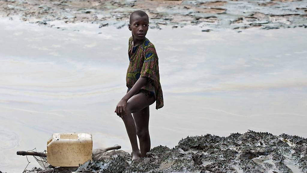 Ein Bub steht mit seinem Fischernetz am ölverschmierten Ufer eines Baches in der Nähe von Goi in Ogoniland.
