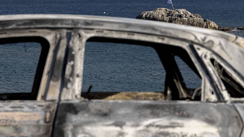 Ein verbranntes Fahrzeug steht am Strand auf der Insel Rhodos. Auch in Mittelgriechenland sind zahlreiche Brände ausgebrochen. Foto: Christoph Reichwein/dpa