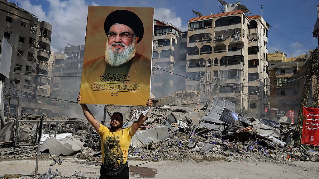 ARCHIV - Ein pro-iranischer Hisbollah-Anhänger hält ein Poster des getöteten Hisbollah-Generalsekretärs Nasrallah vor einem Gebäude hoch, das bei einem israelischen Luftangriff auf einen südlichen Vorort von Beirut zerstört wurde. Foto: Marwan Naamani/dpa