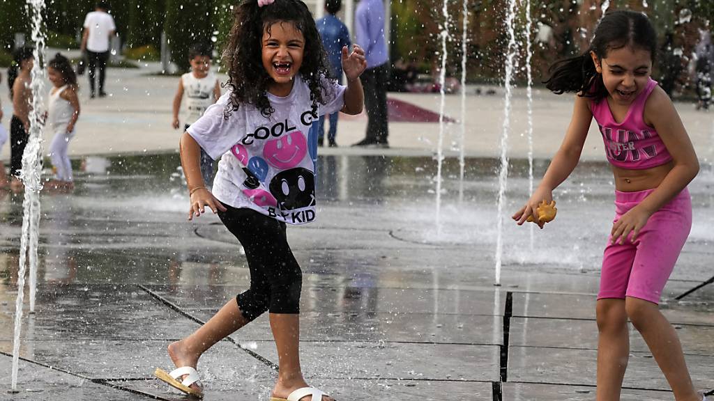 Kinder spielen am 1. August bei Temperaturen von rund 38 Grad Celsius unter einer Wasserfontäne im Ebrahim-Park. Foto: Vahid Salemi/AP/dpa