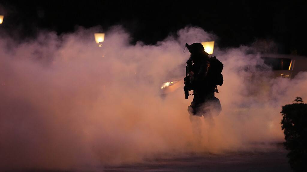 Ein Polizist geht durch Rauch während einer Demonstration gegen die Corona-Impfungen und weiteren Maßnahmen zur Eindämmung der Pandemie. Foto: Petr David Josek/AP/dpa