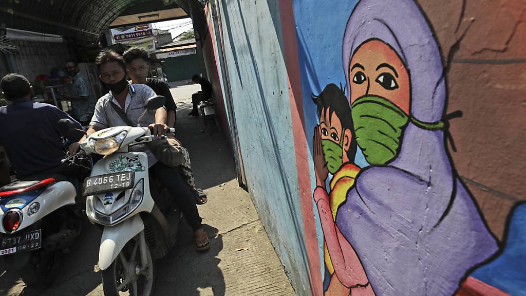 Ein Wandbild in Jakarta zeigt eine Frau und ein Kind, die Mundschutz tragen. Foto: Dita Alangkara/AP/dpa