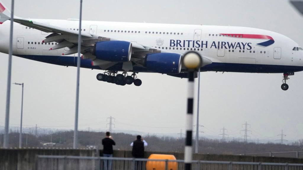 ARCHIV - Menschen beobachten die Landung eines Flugzeugs der British Airways in London. Foto: Kin Cheung/AP/dpa/Archivbild