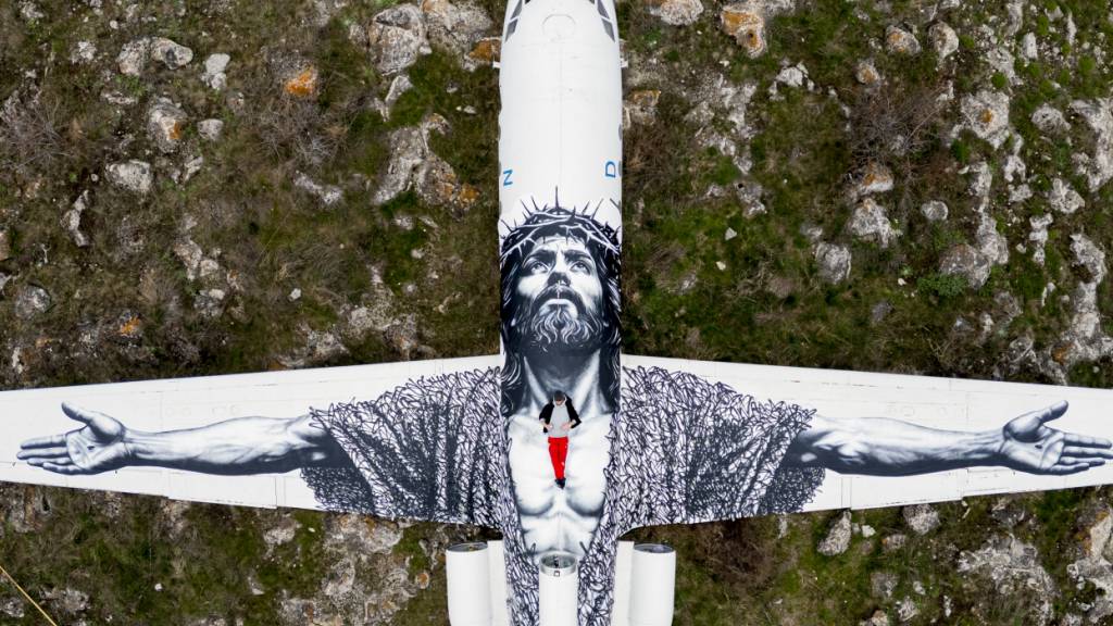 Der Berner Künstler Vierwind alias Micha Haeni in roter Hose auf seinem Kunstwerk: der gekreuzigte Christus, gemalt auf auf ein Flugzeug und betrachtet aus der Himmelsperspektive. Für Haeni symbolisiert es, dass an Himmelfahrt Gott herabsteigt zu den Menschen.