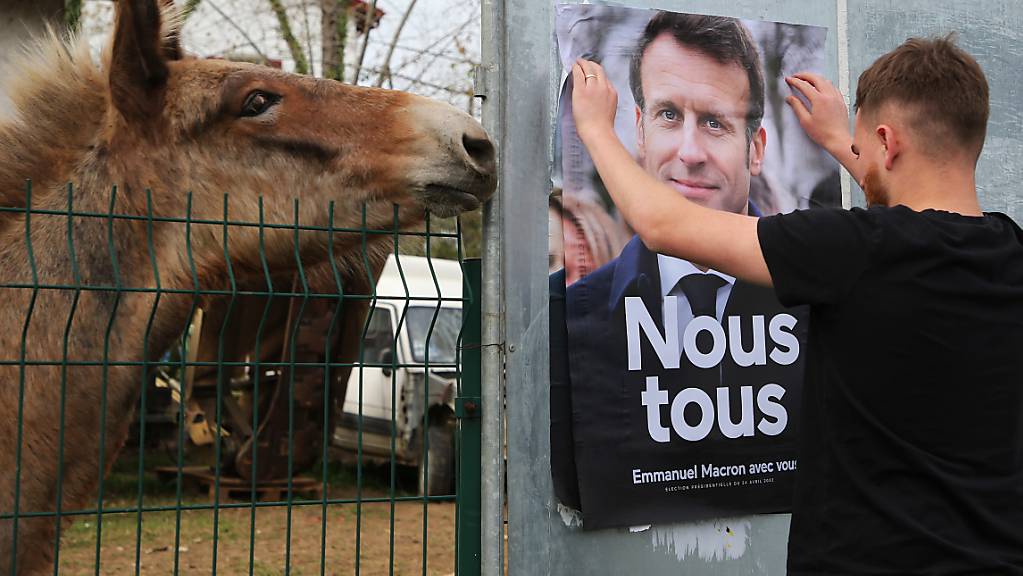 Ein Mann klebt ein Wahlkampfplakat des französischen Präsidenten und Präsidentschaftskandidaten Macron auf. Die Sozialistische Partei will die Gesellschaft mit markigen Sprüchen zur Wiederwahl von Emmanuel Macron mobilisieren. Foto: Bob Edme/AP/dpa