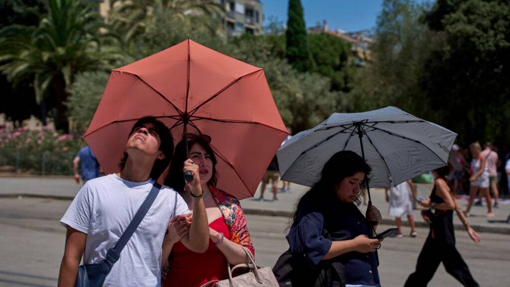 Touristen schützen sich an einem heißen Tag vor der Kirche Sagrada Familia in Barcelona mit Regenschirmen vor der Sonne. Foto: Emilio Morenatti/AP/dpa