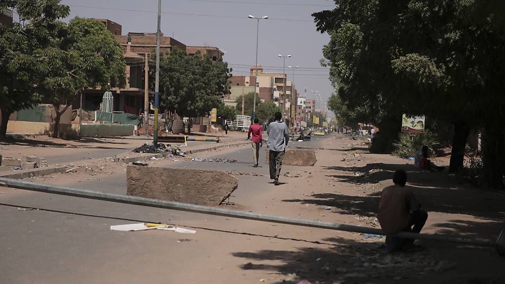Personen gehen auf einer Straße, auf der Steine als behelfsmäßigen Barrikade liegen. Foto: Marwan Ali/AP/dpa