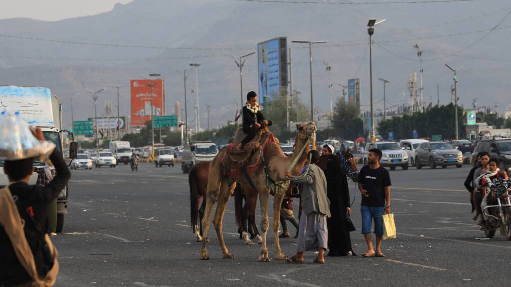 ARCHIV - Ein Junge reitet auf einem Kamel, während sich Menschen entlang einer Straße versammeln. Foto: Osamah Abdulrahman/AP/dpa