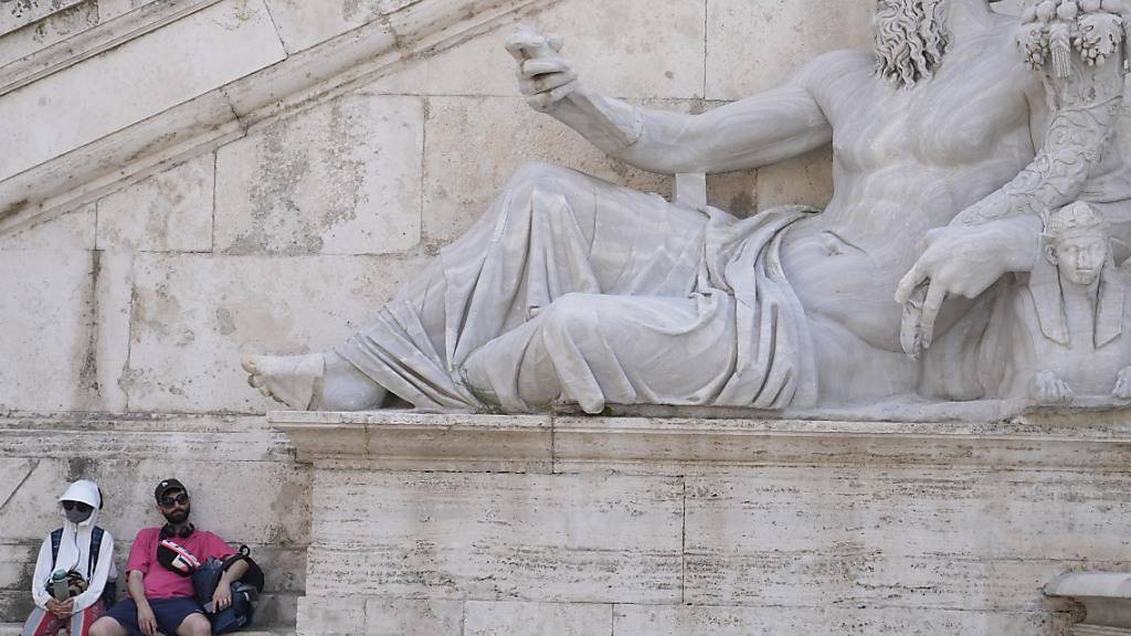 Zwei Touristen ruhen sich im Schatten auf der Piazza del Campidoglio in Rom aus. Es soll wieder sehr heiß werden in Italien. Foto: Gregorio Borgia/AP/dpa