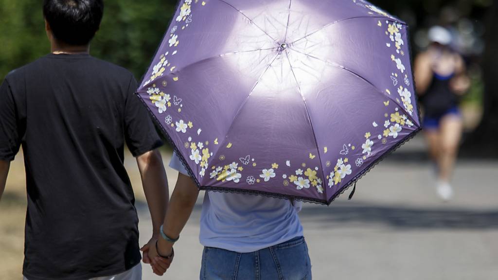 Schutz vor der Sommerhitze unter einem Schirm auf einem Spaziergang in Genf. (Archivbild)
