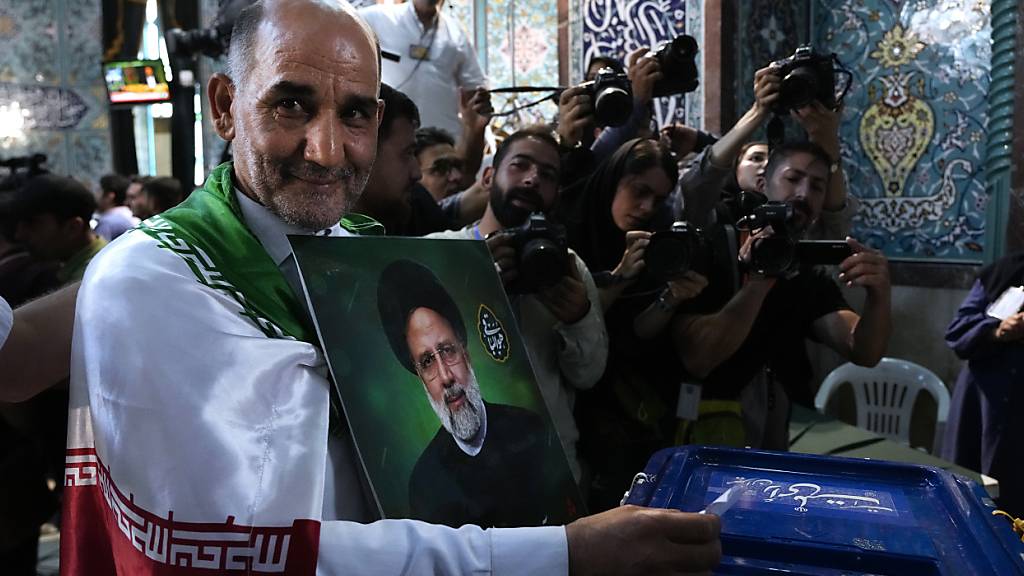 dpatopbilder - Ein Mann gibt während der Präsidentenwahlen seine Stimme ab, während er ein Bild des verstorbenen Präsidenten Ebrahim Raisi in einem Wahllokal in der Hand hält. Rund 61 Millionen Wählerinnen und Wähler sind in der Islamischen Republik dazu aufgerufen, einen neuen Regierungschef zu wählen. Foto: Vahid Salemi/AP