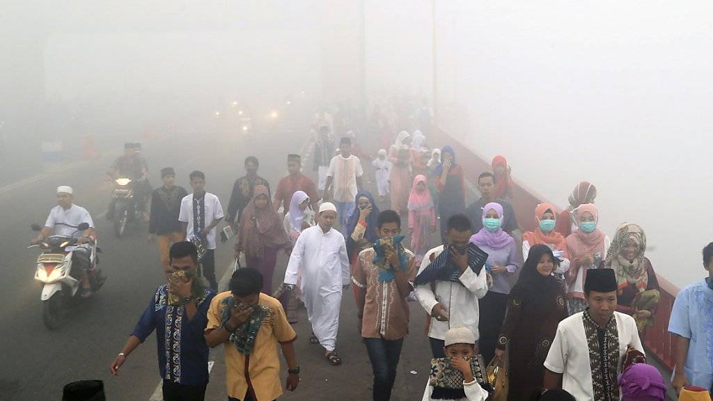 Stark eingeschränkte Sicht: Muslime auf Sumatra gehen zum Morgengebet - wegen des starken Rauchs tragen viele Gesichtsmasken oder halten sich Tücher vor Nase und Mund.