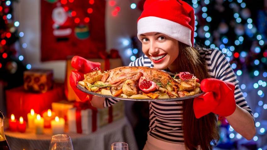 Smiling woman with turkey garnished with potato and garnet dressed with Christmas hat on festive light background