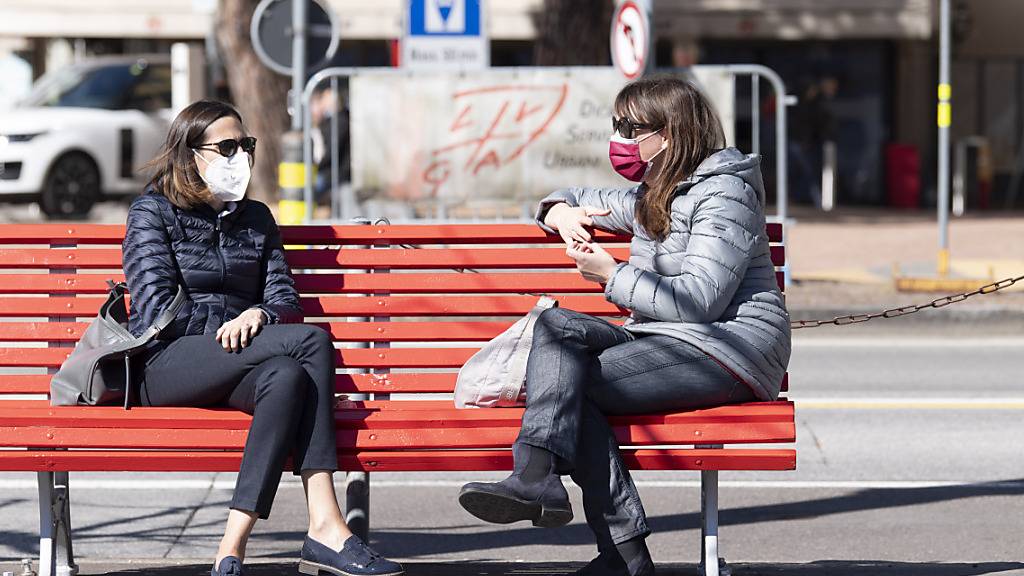 Schutzmasken gehören mittlerweile zum Alltag, so wie hier in Lugano, wo zwei Frauen auf einer Sitzbank verweilen. (Themenbild)