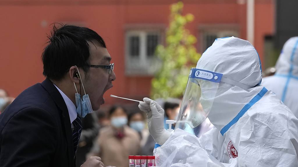 Ein Angestellter (l) öffnet den Mund für einen Coronavirus-Test vor einem Hotel im chinesischen Bezirk Haidian. Foto: Ng Han Guan/AP/dpa