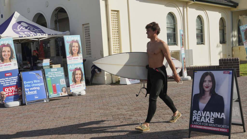 Ein Surfer trägt sein Brett, während er an einer Wahlkabine am Bondi Beach in Sydney vorbeigeht. Foto: Mark Baker/AP/dpa