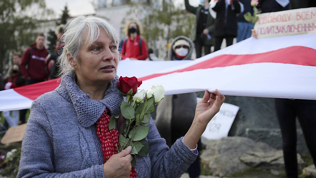 Eine Frau hält bei einer Demonstration Rosen und die historische weiss-rot-weisse Fahne in der Hand. Tausende Menschen, darunter vor allem Senioren und Studenten, marschierten am Montag durch die Hauptstadt.