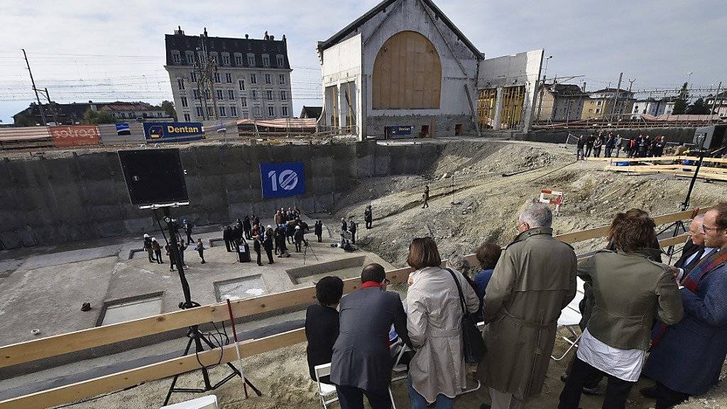 Das Publikum beobachtet vom Rand der Grube aus, wie in der Mitte der Baustelle der mit Kunstwerken gefüllte symbolische Grundstein des neuen kantonalen Kunstmuseum in Lausanne gelegt wird.