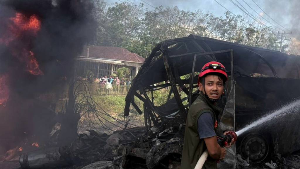 dpatopbilder - HANDOUT - Ein Retter versucht das Feuer zu löschen, nachdem ein Passagierbus mit einem Tankwagen in der Provinz Süd-Sumatra zusammengestoßen ist. Foto: Uncredited/South Sumatra Regional Police/AP/dpa - ACHTUNG: Nur zur redaktionellen Verwendung im Zusammenhang mit der aktuellen Berichterstattung und nur mit vollständiger Nennung des vorstehenden Credits