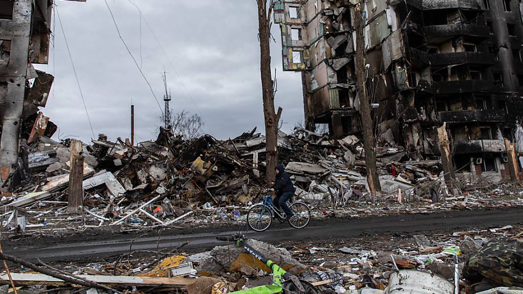 Ein Mann fährt auf einem Fahrrad an einem zerstörten Wohnhaus in der Stadt Borodjanka vorbei. Der ukrainische Innenminister Denys Monastyrskyj hat ukrainische Medien am Donnerstagmorgen von großen Zerstörungen in der Kleinstadt Borodjanka bei Kiew berichtet. Foto: Alex Chan/SOPA Images via ZUMA Press Wire/dpa