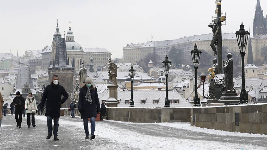 Menschen überqueren die mittelalterliche Karlsbrücke nach dem ersten Schneefall in Prag am ersten Tag der Lockerungen der Corona-Maßnahmen in Tschechien nach einem Lockdown. Am Donnerstag durften alle Geschäfte, Einkaufszentren, Restaurants, Bars und Hotels wieder öffnen. Foto: Petr David Josek/AP/dpa