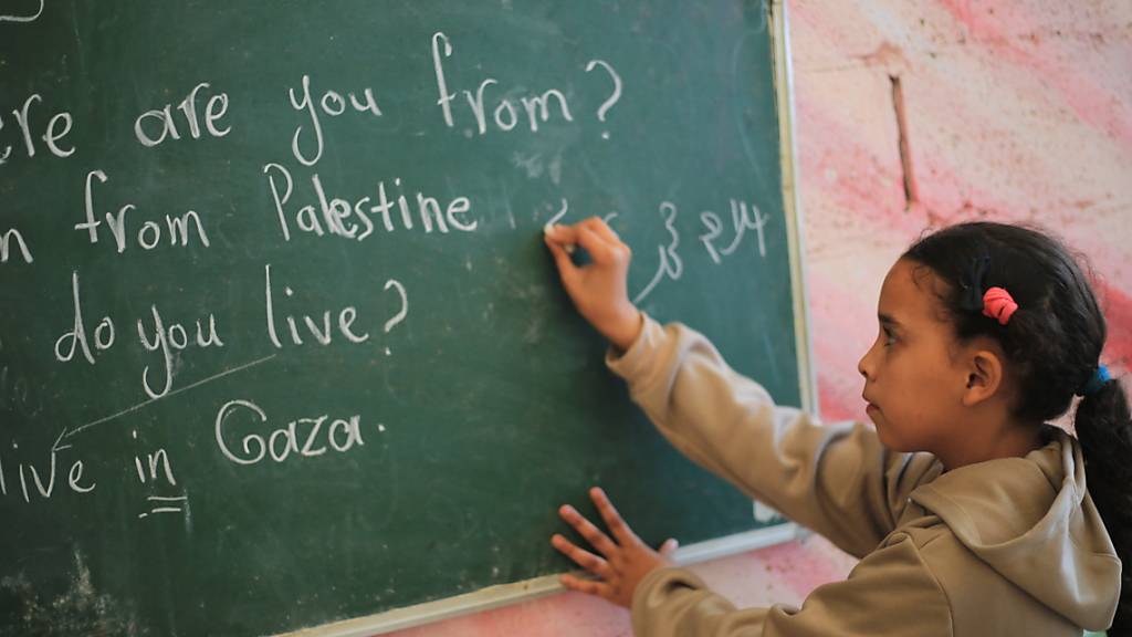 Ein palästinensisches Mädchen schreibt an eine Tafel. Wegen des Gaza-Krieges mangelt es im Gazastreifen an Bildungsmitteln. Foto: Mohammed Talatene/dpa