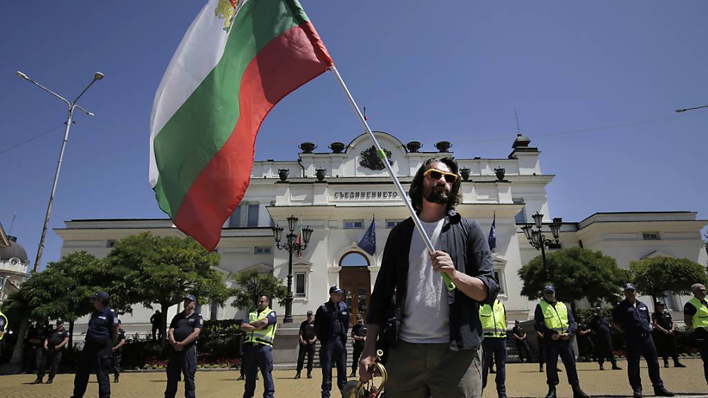 Ein Mann hält während einer Protestaktion vor dem bulgarischen Parlament die Fahne des Landes. Foto: Valentina Petrova/AP/dpa