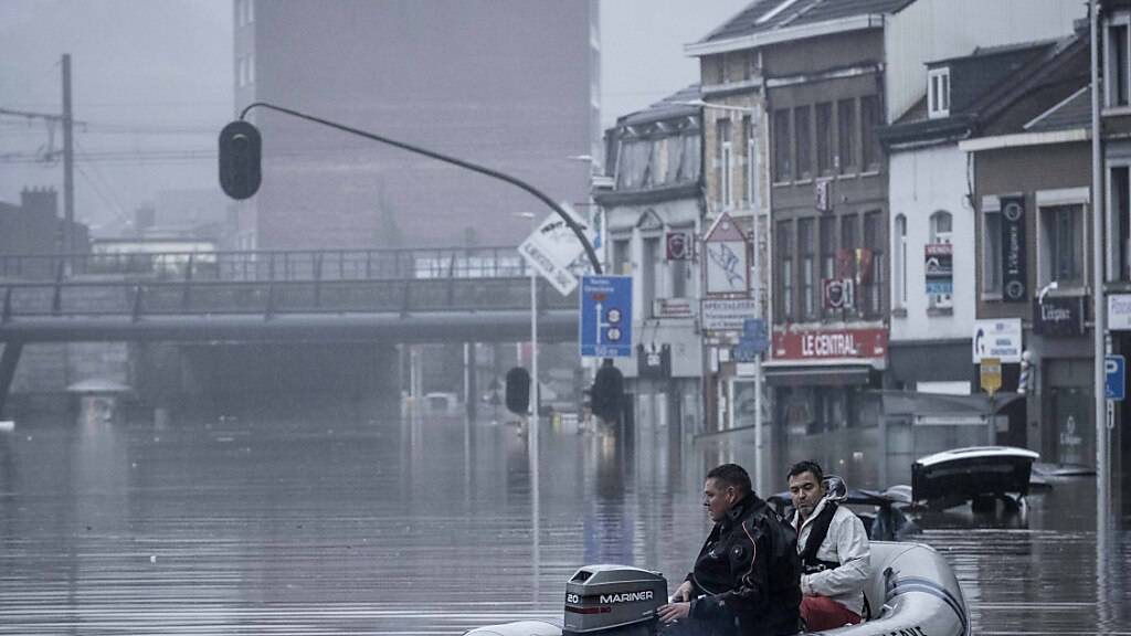 Zwei Männer nutzen ein Gummiboot im Wasser, nachdem die Maas bei schweren Überschwemmungen über die Ufer getreten ist. Foto: Valentin Bianchi/AP/dpa