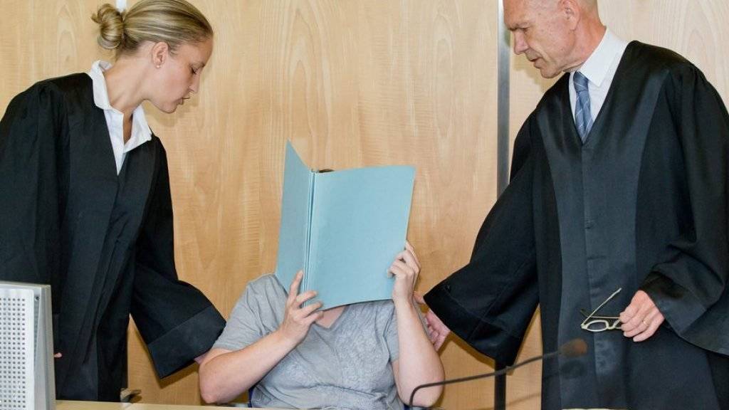 Die Mutter von acht toten Babys in Bayern muss für 14 Jahre hinter Gitter. Das Bild zeigt die 45-Jährige, die vor Gericht ihr Gesicht mit einem Aktenordner verdeckt, zusammen mit ihren Anwälten.