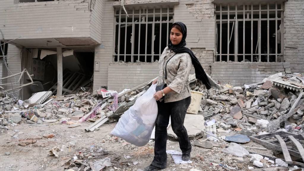 ARCHIV - Eine Frau holt Kleidung in einer Tüte aus einem Wohnhaus, das am vergangenen Montag (09.03.2026) während der US-israelischen Luftangriffe beschädigt wurde. Foto: Vahid Salemi/AP/dpa
